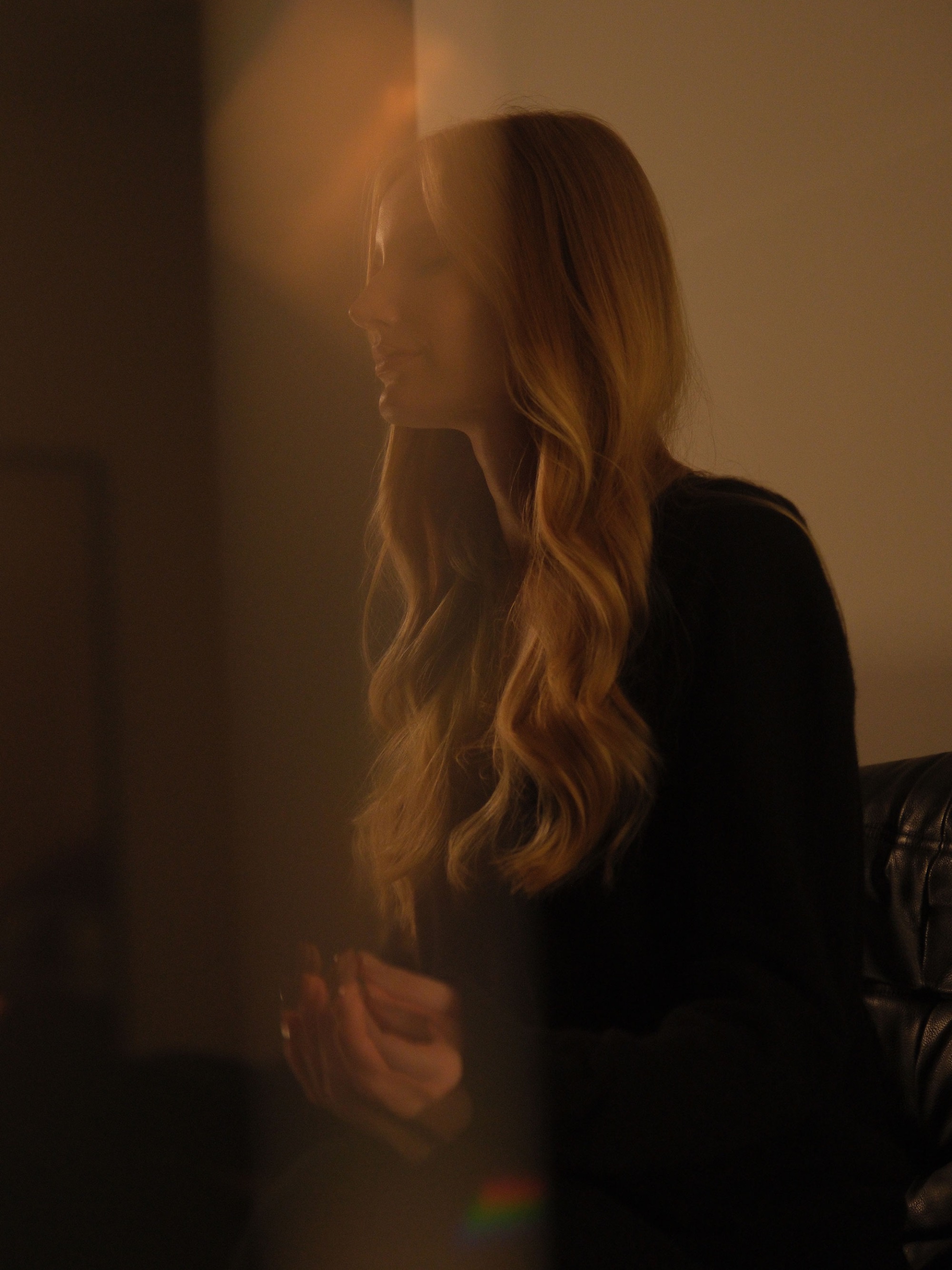 Woman with long blonde hair seated in soft golden light, eyes closed in a calm, reflective moment.