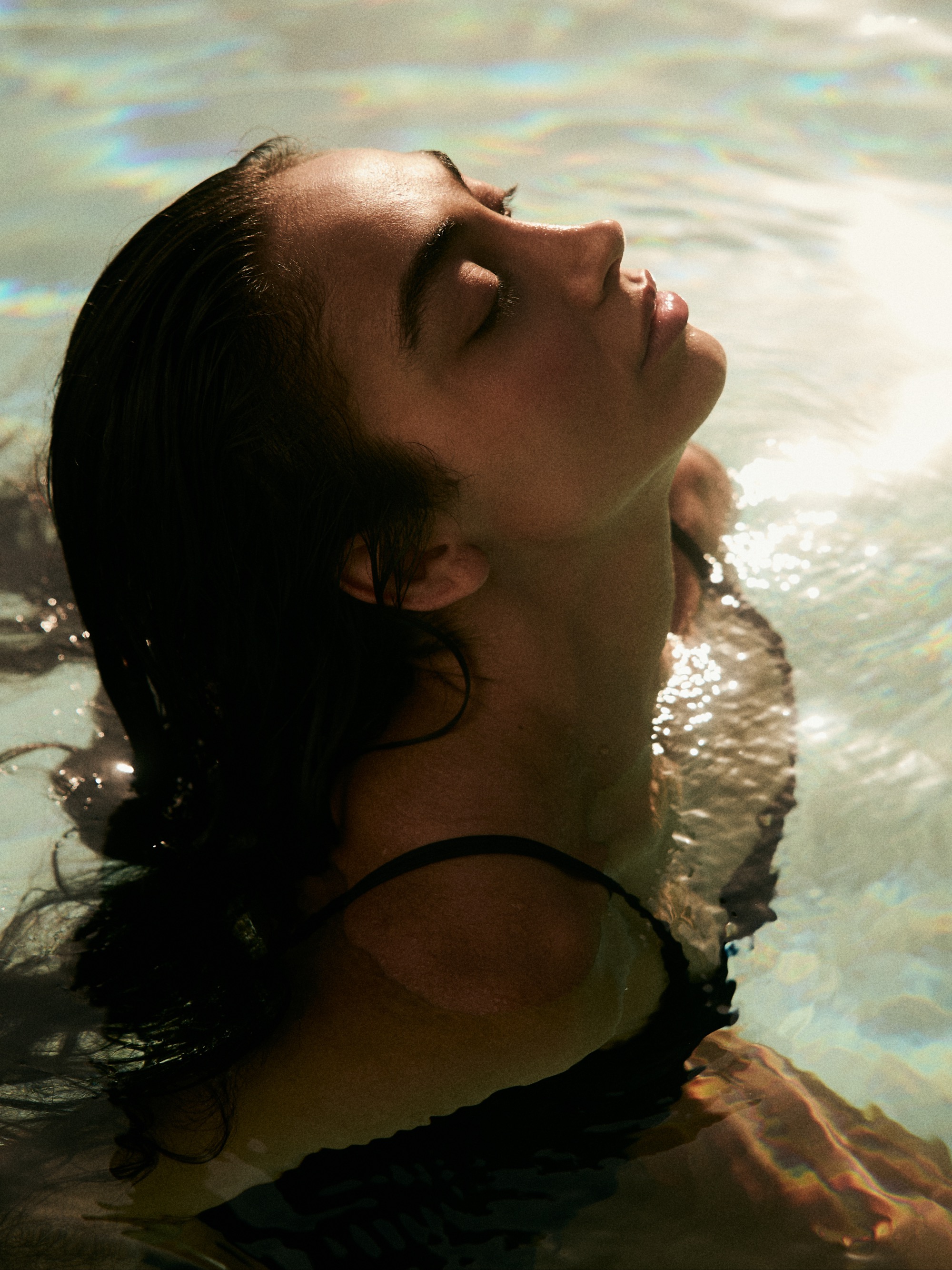 Woman with long brunette hair relaxes in a pool of water and sunlight