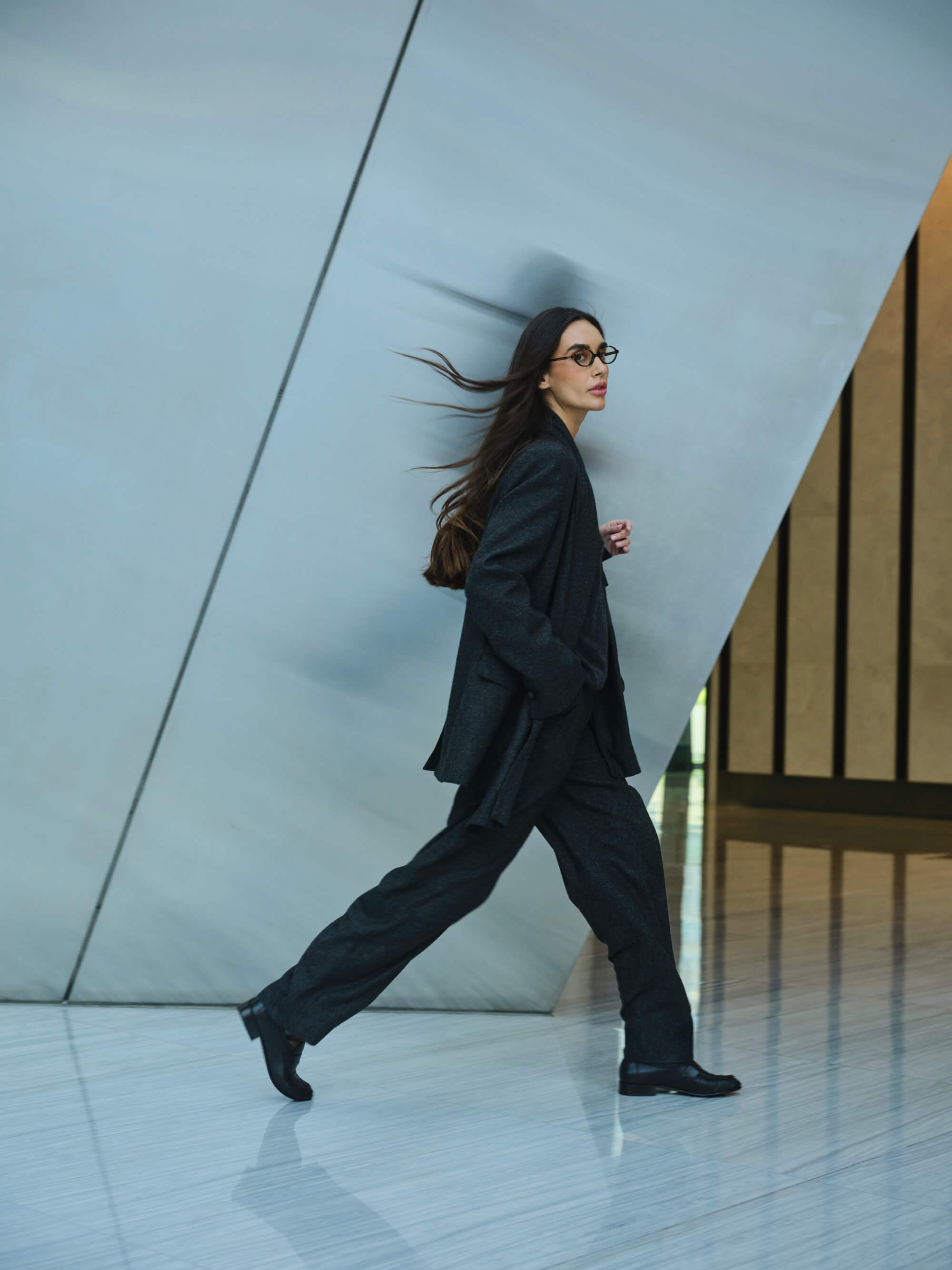 A woman looks at the camera whilst walking in a black power suit.