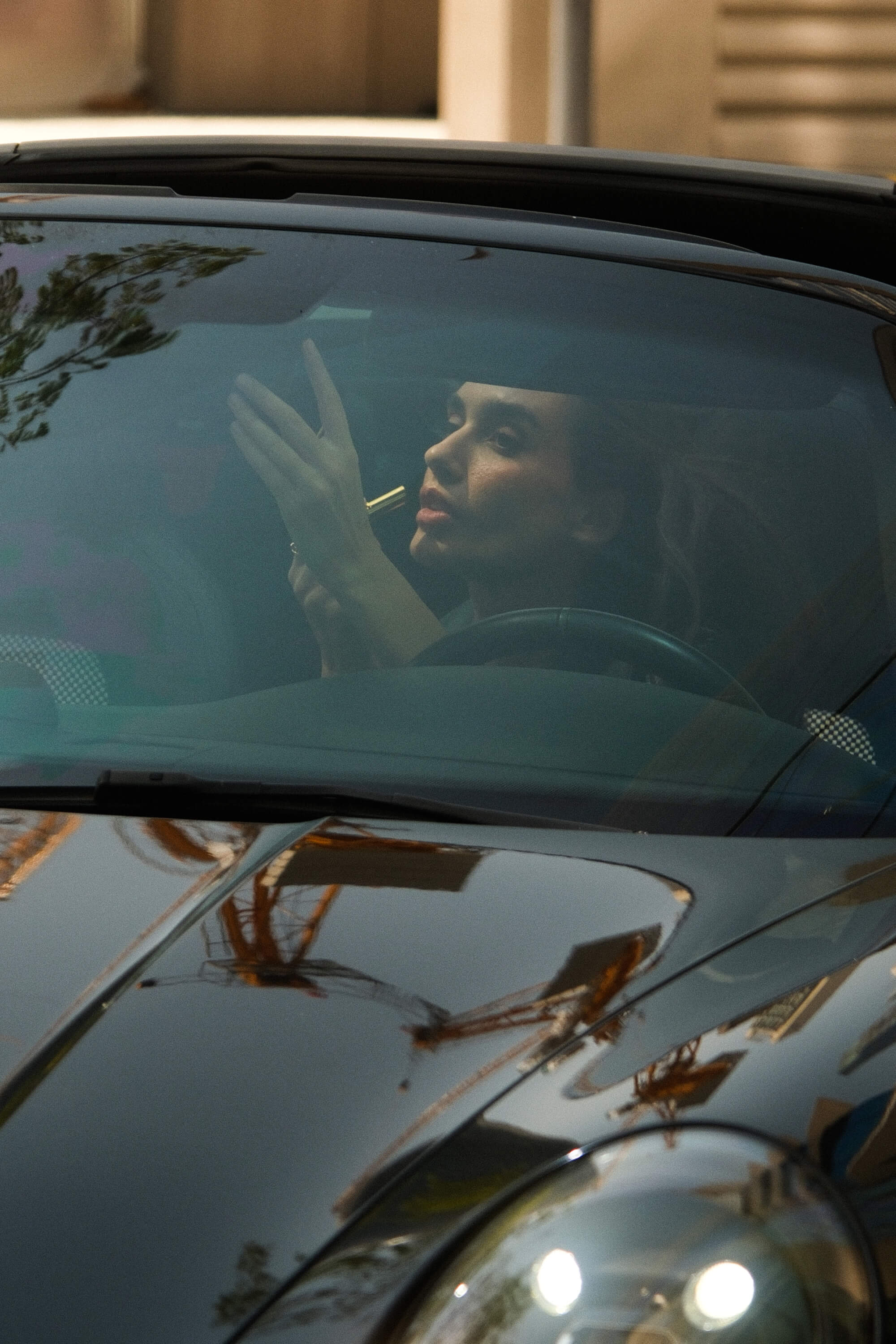 A woman looks in her car rearview mirror to put on lipstick.