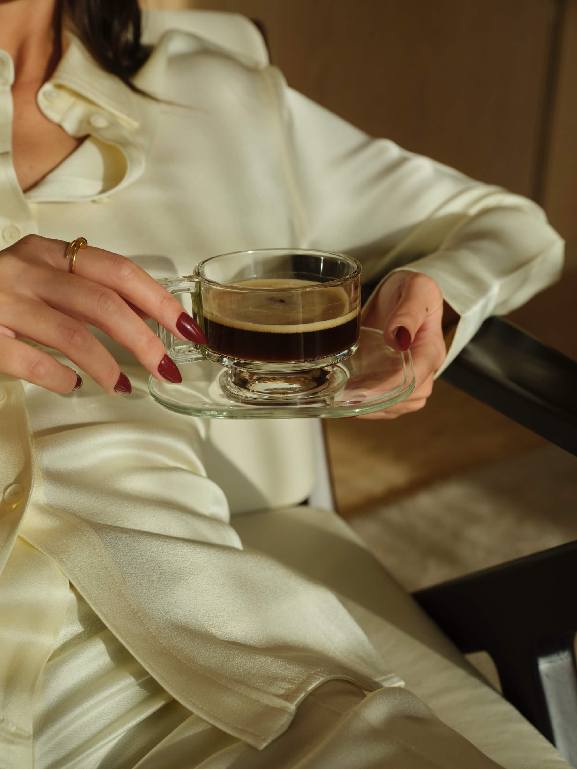 Close up of a woman in a white suit holding a glass coffee cup filled with coffee.  how the welltth app helps to elevate your energy everyday